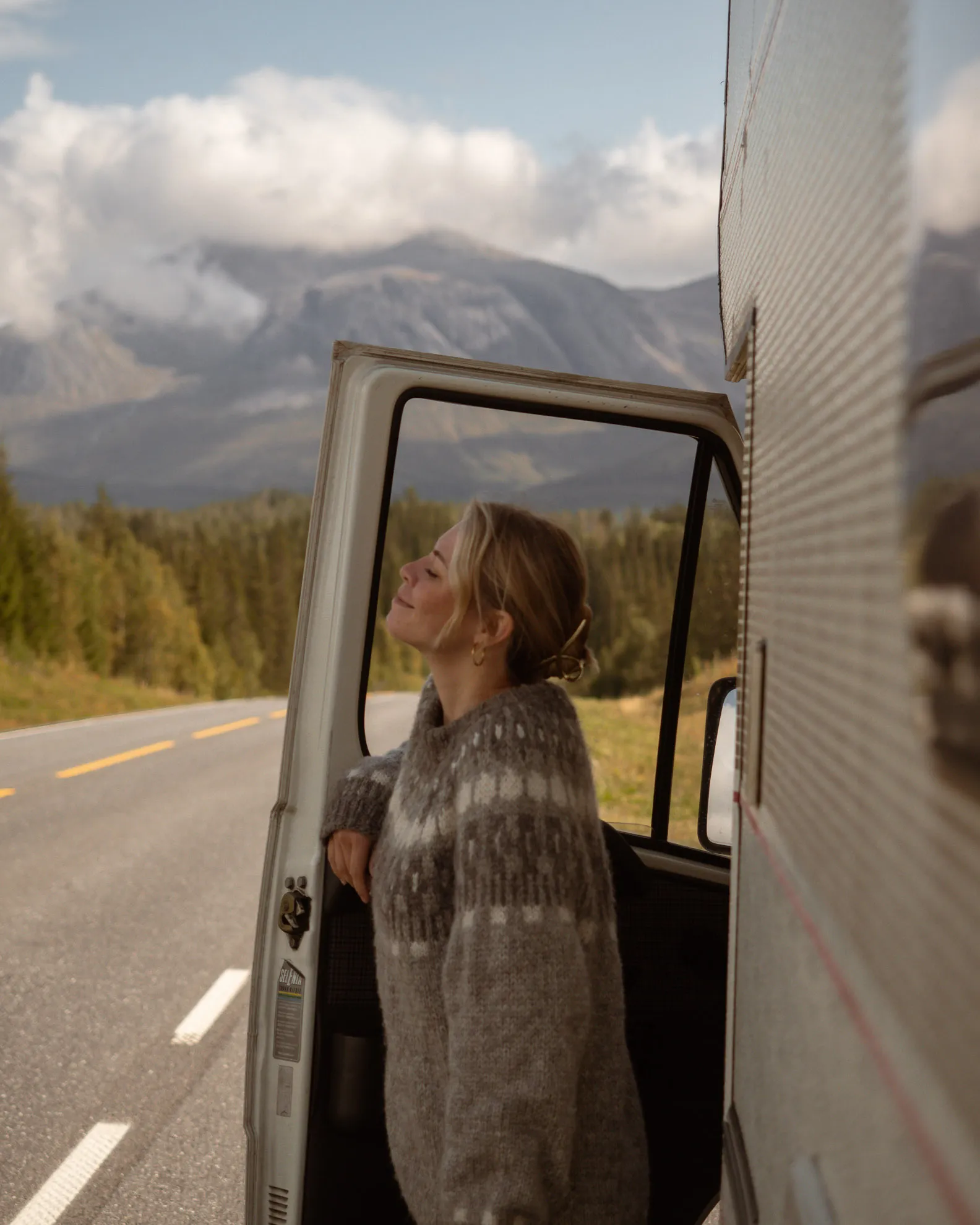 Vanessa von Be a Hyggespreder steigt aus einem Van aus, im Hintergrund Berge, Wolken und eine breite Straße