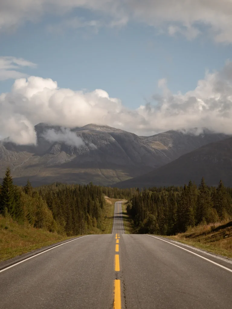 Eine verlassene Straße in Norwegen mit gelbem Mittelstreifen und Bergen und Wolken im Hintergrund